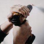 Hands holding a drill closely on a white wall, focusing on home improvement.