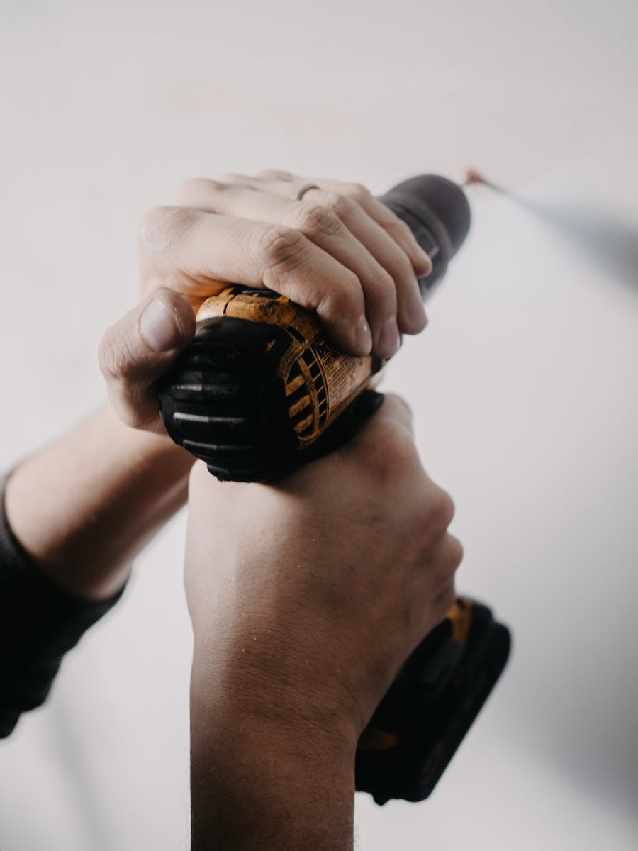 Hands holding a drill closely on a white wall, focusing on home improvement.