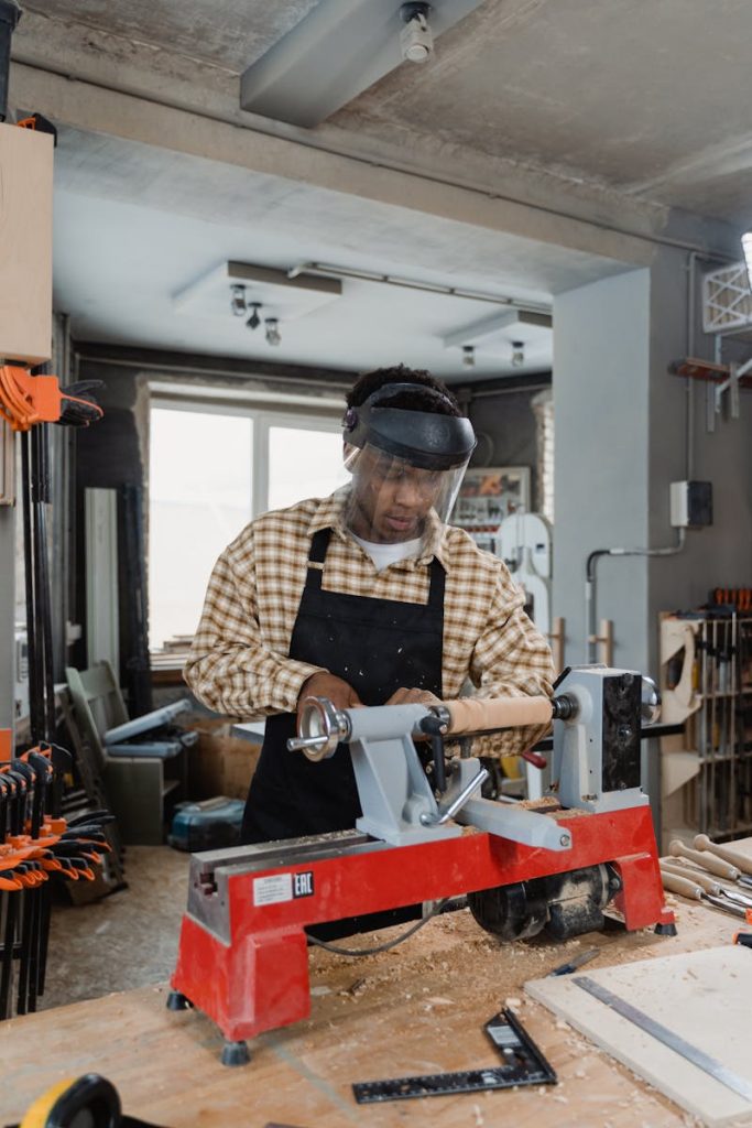 Man Wearing Checkered Long Sleeves and an Apron in a Workshop working on a lathe